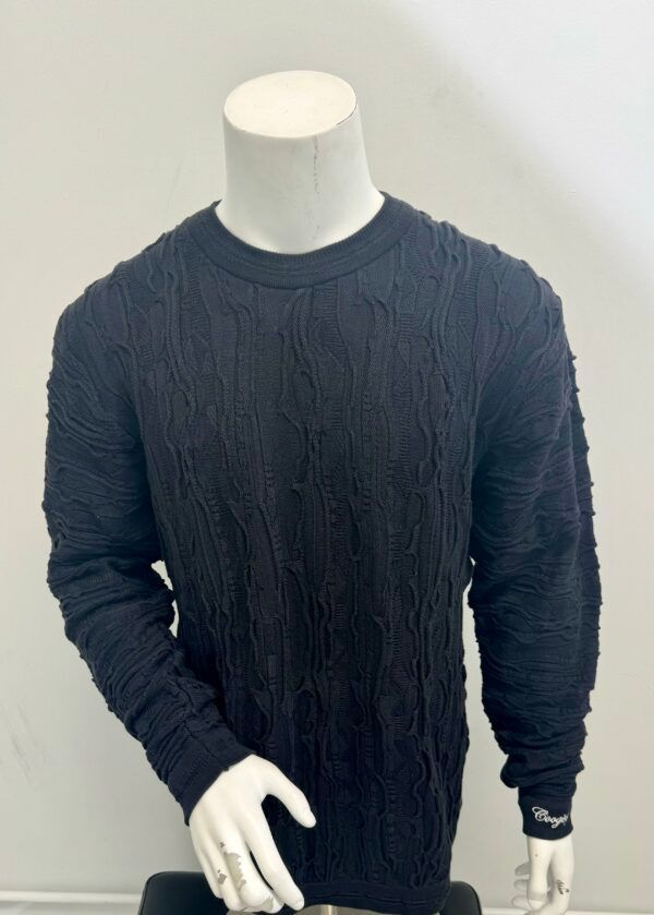 A black sweater is on a mannequin against a white wall