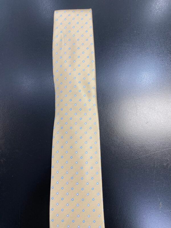 A yellow tie with blue polka dots is sitting on a black table.