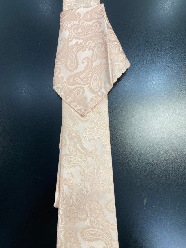 A tie with a paisley pattern is hanging on a black wall