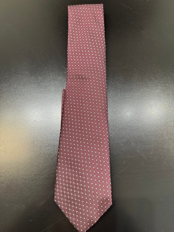 A burgundy tie with white polka dots is sitting on a black table.