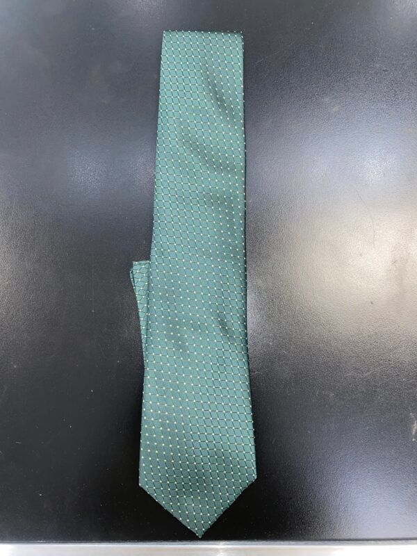 A green tie with white polka dots is sitting on a black table.