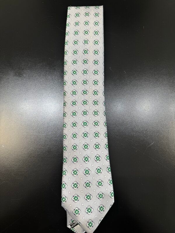 A white tie with green squares on it is sitting on a black table.