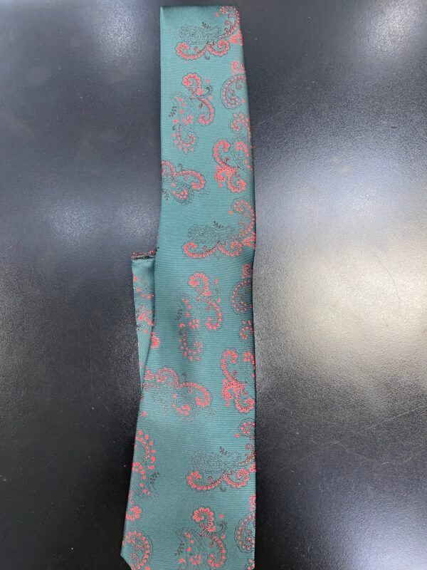 A green tie with a pink paisley pattern is sitting on a black table.