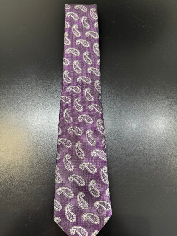 A purple tie with white paisley on it is sitting on a black table.