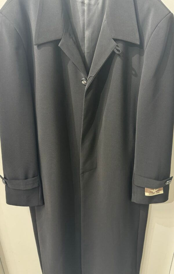 A black coat is hanging on a white wall.
