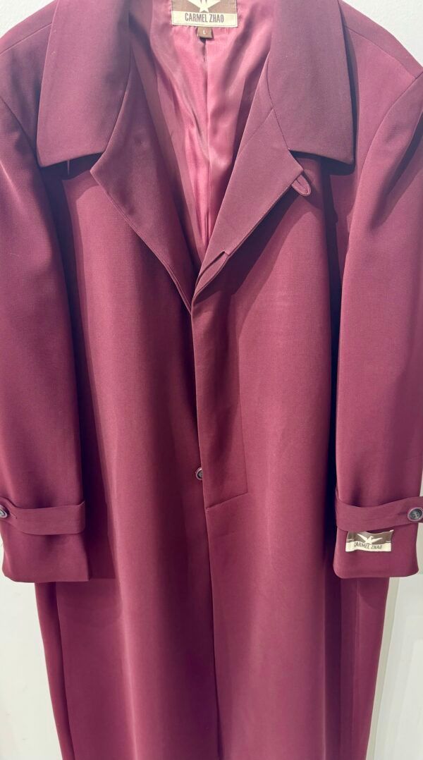 A burgundy coat is hanging on a white wall.