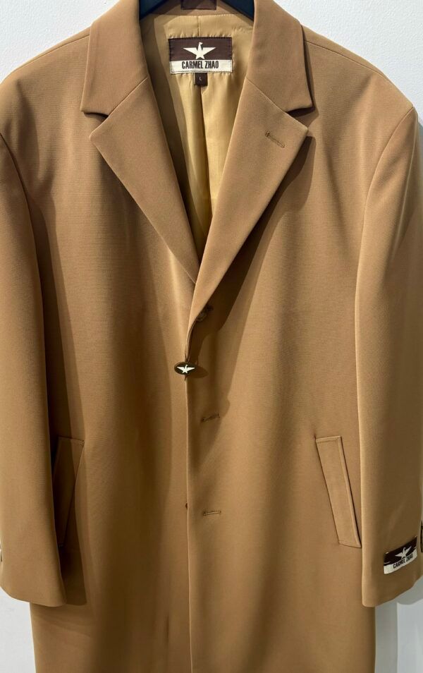 A tan coat is hanging on a hanger on a white wall.
