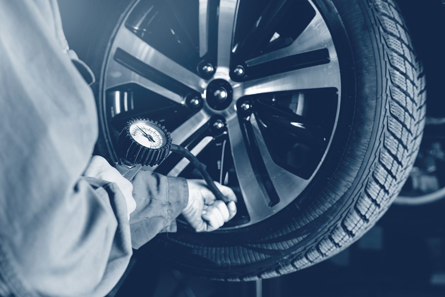Mechanic inflating a car tire with a gauge in a garage, close-up.