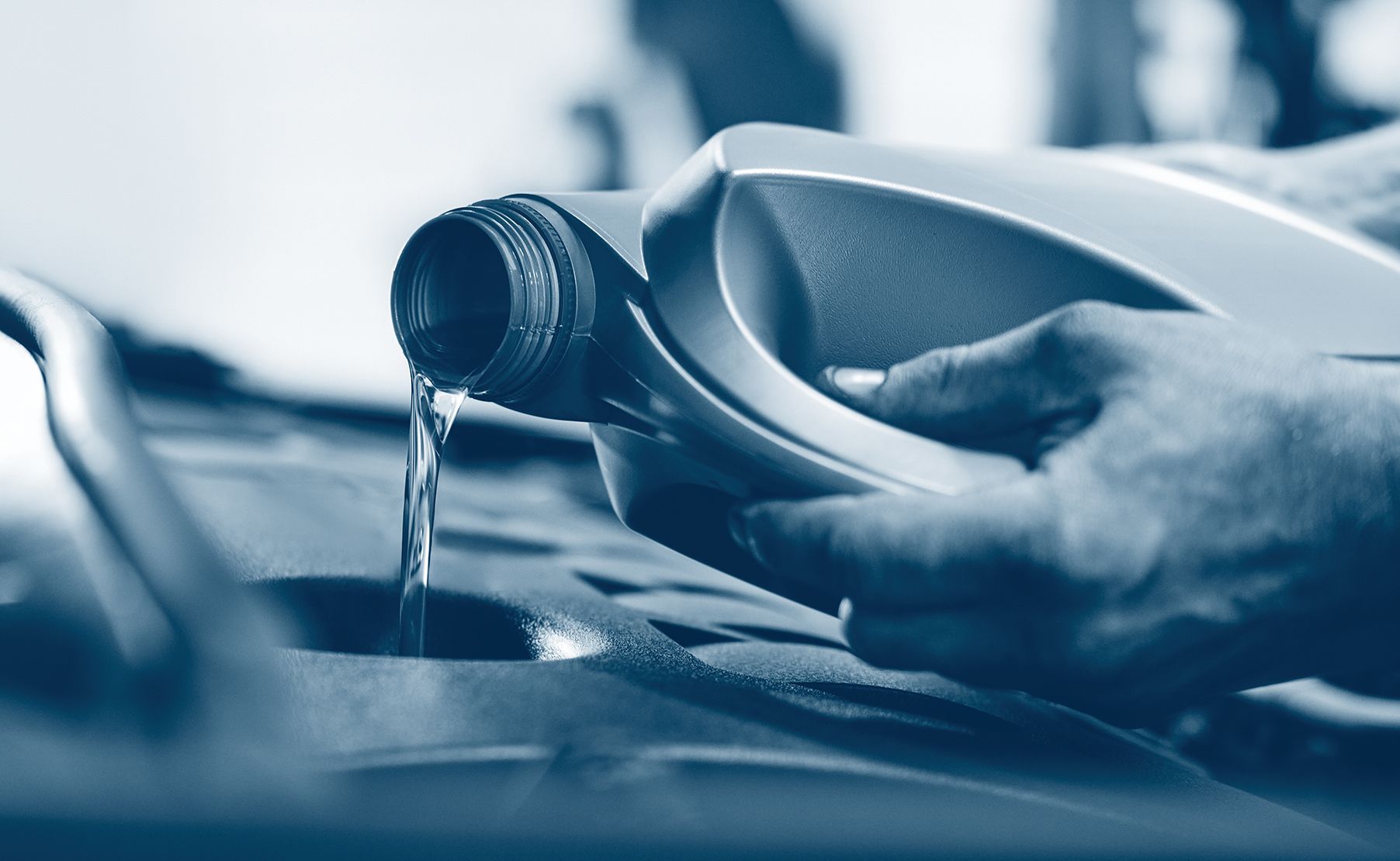 A person pouring motor oil into a car engine from a plastic container.