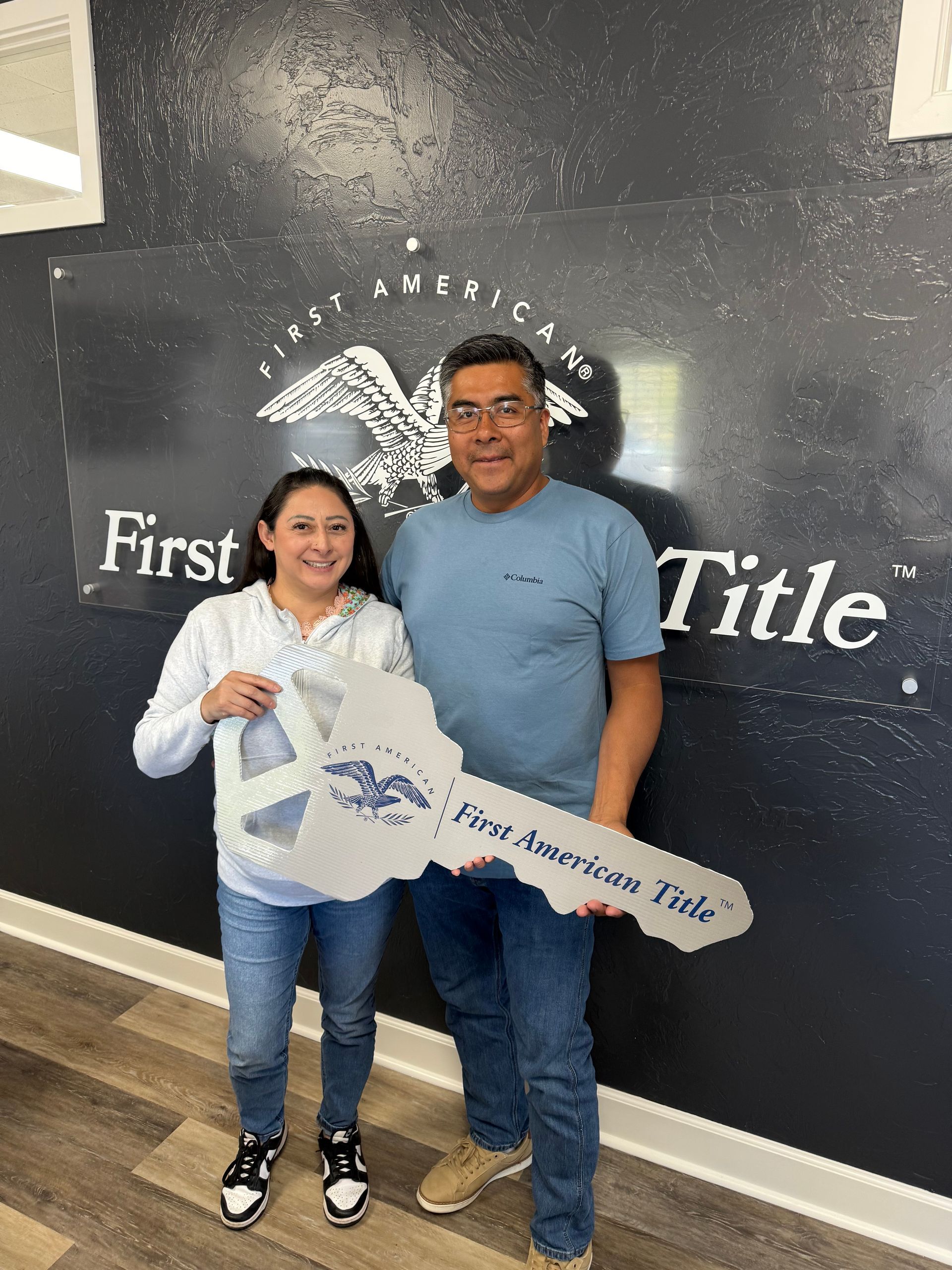 A couple holding a giant key in front of a First American Title sign.