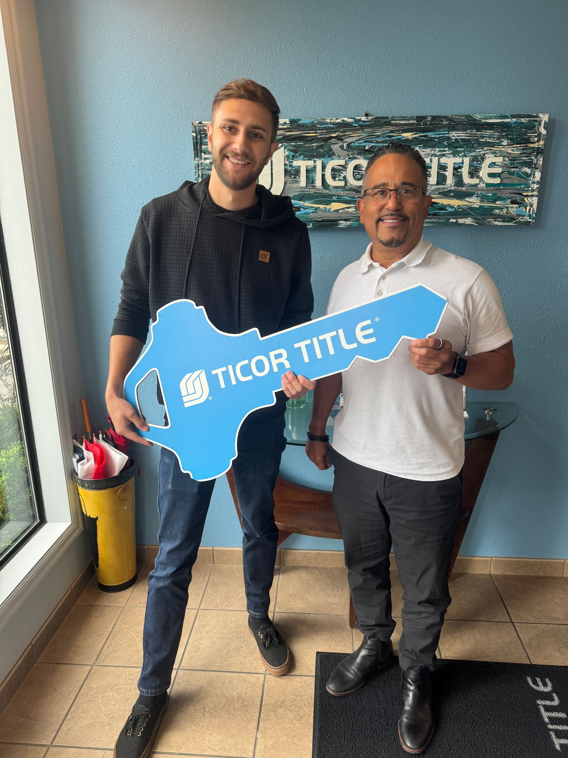 Two men holding a large blue key that says "Ticor Title." They are inside an office.