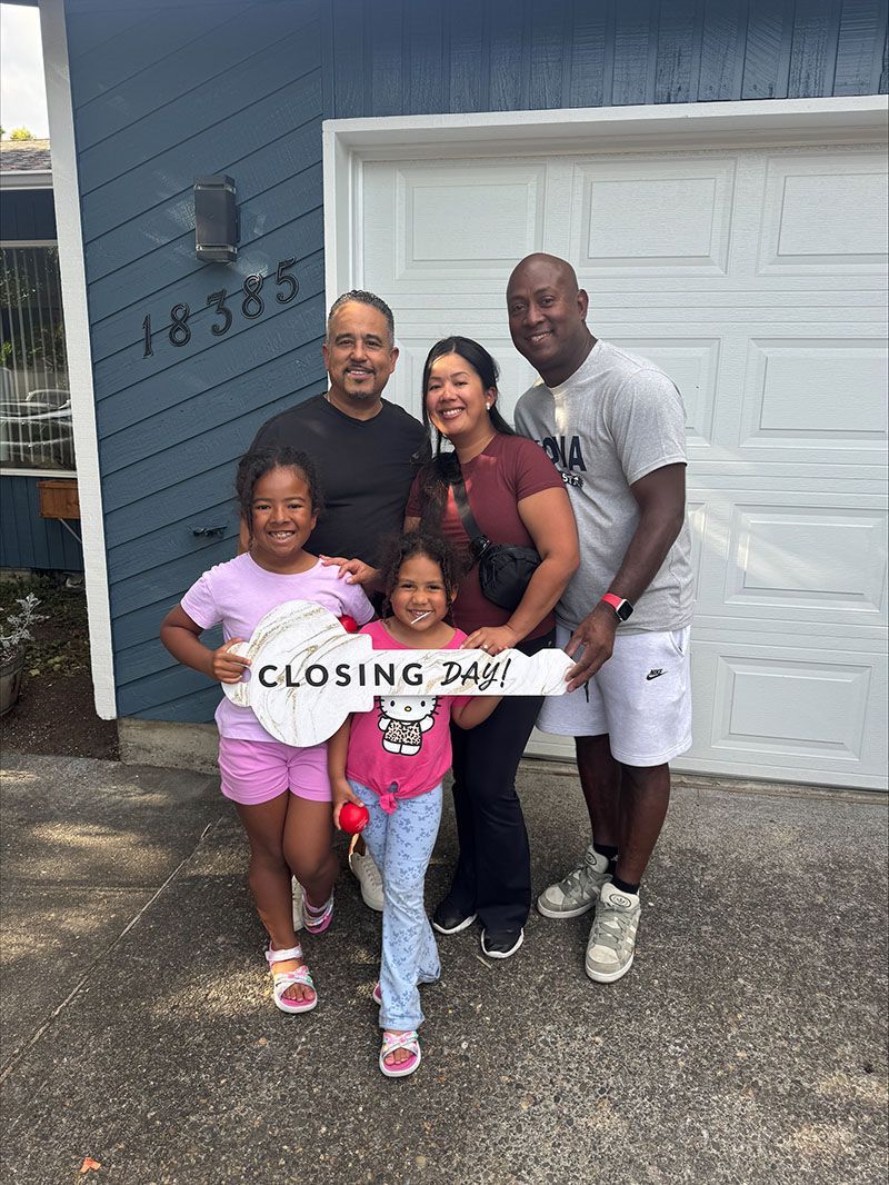 Family of five holding oversized key in front of new home, jubilant expressions.