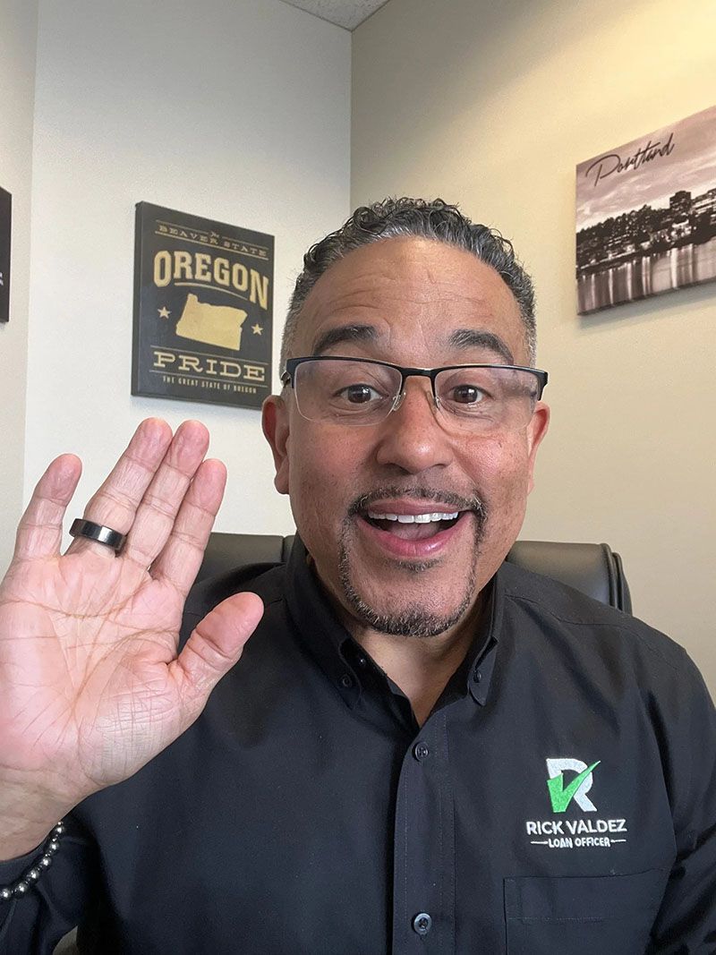 Man in glasses waves, smiling, in front of an 