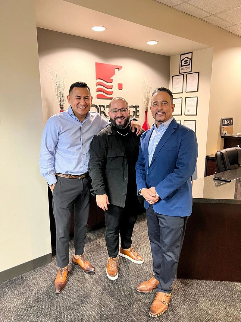 Three men stand in an office. They are smiling. The logo of a company is in the background.