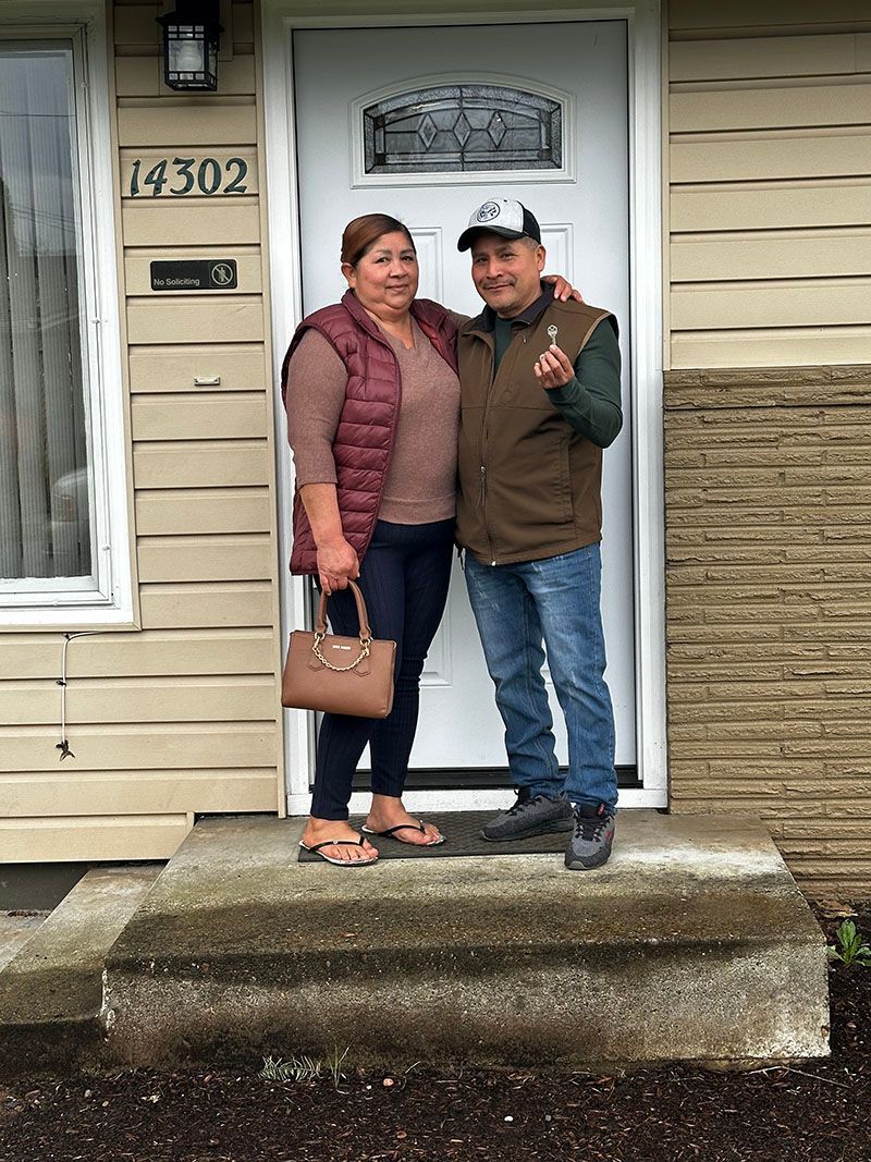 Couple standing on front steps, holding key, in front of a house.