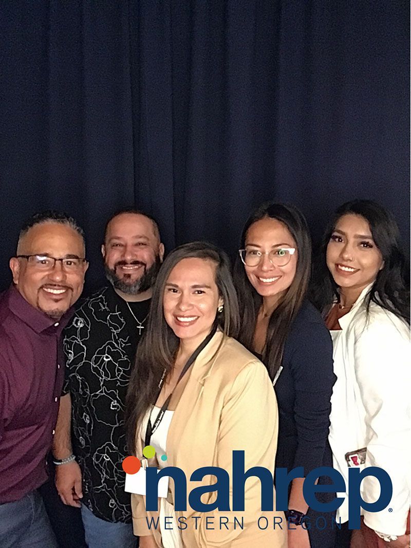 Five people smiling in front of a dark blue backdrop, with an organization's logo on the bottom right.