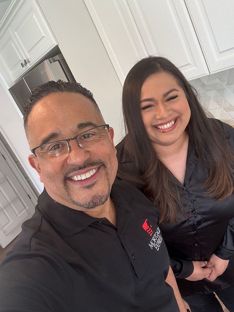 Two smiling people; man wearing glasses and a black shirt, and woman with long brown hair, in a kitchen.