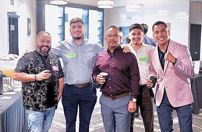 Five men in business attire pose for a photo at an event, smiling, holding drinks, and with arms around each other.