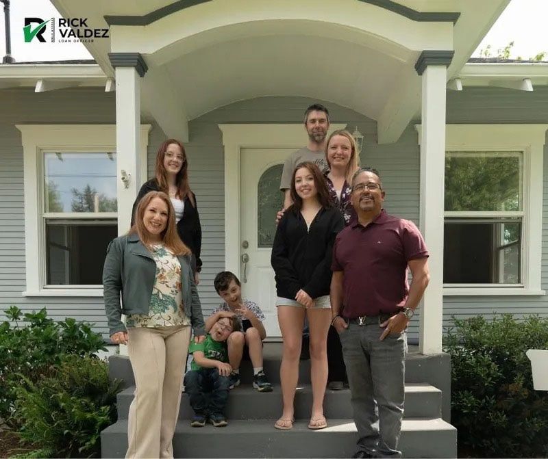 Family poses on front steps of house; smiling, sunny day.