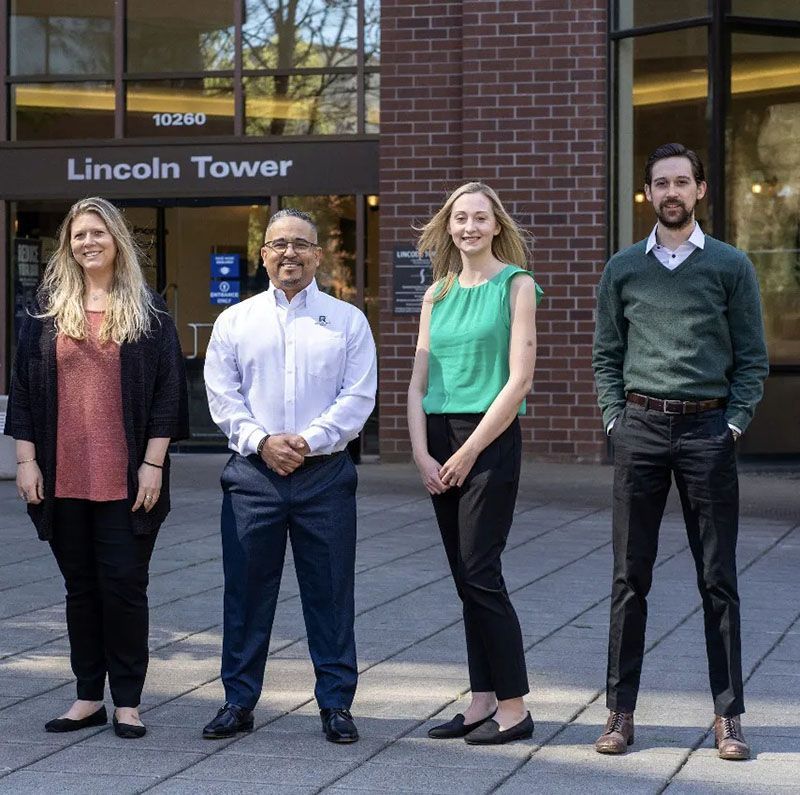 Four people standing in front of a building called Lincoln Tower. Two women and two men smiling, in business casual attire.