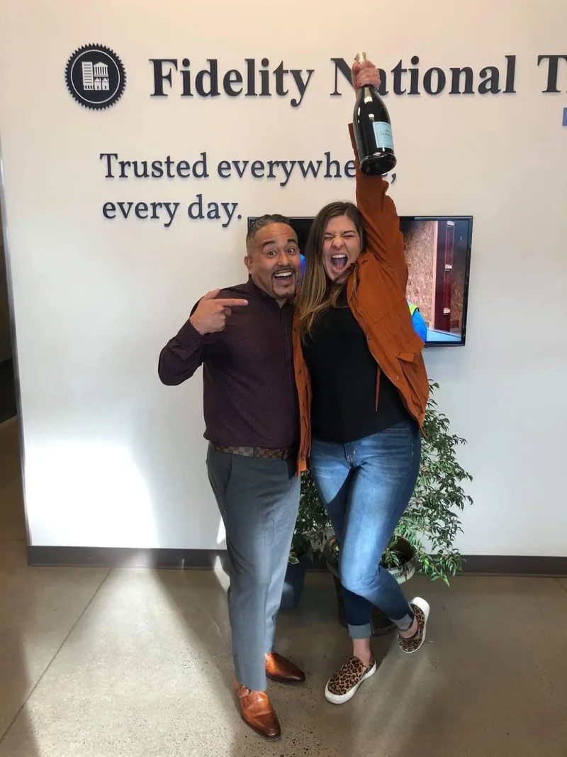 Man points at woman holding champagne bottle, celebrating in front of a 