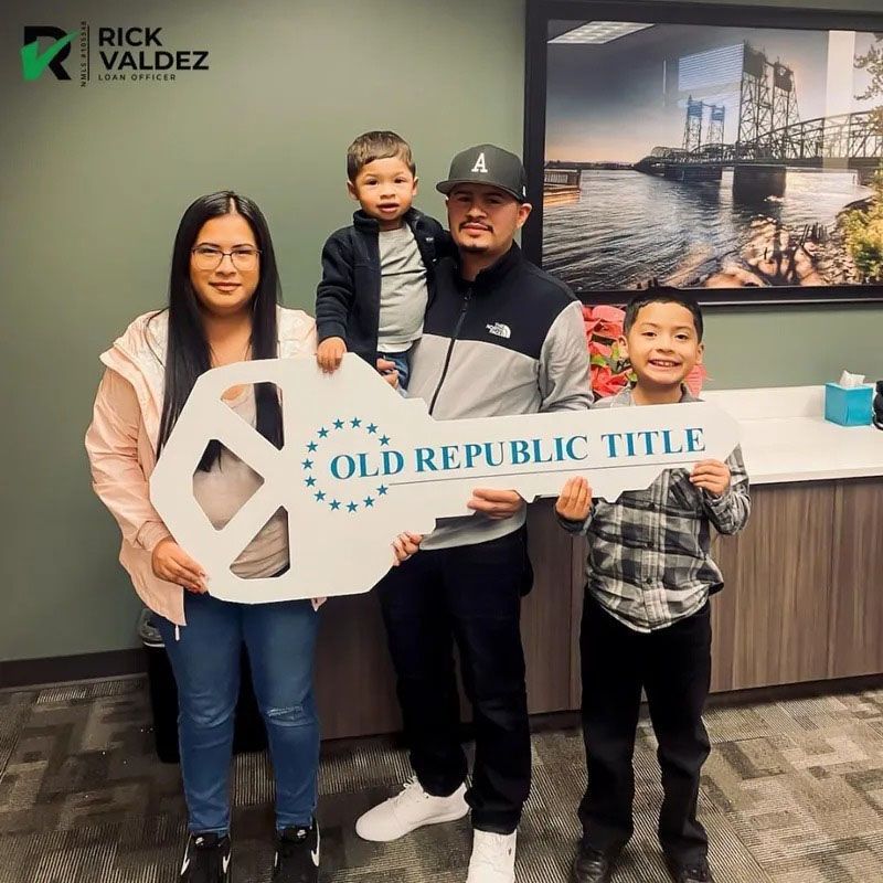 Family holding giant key celebrating a new home in front of a window and office art.