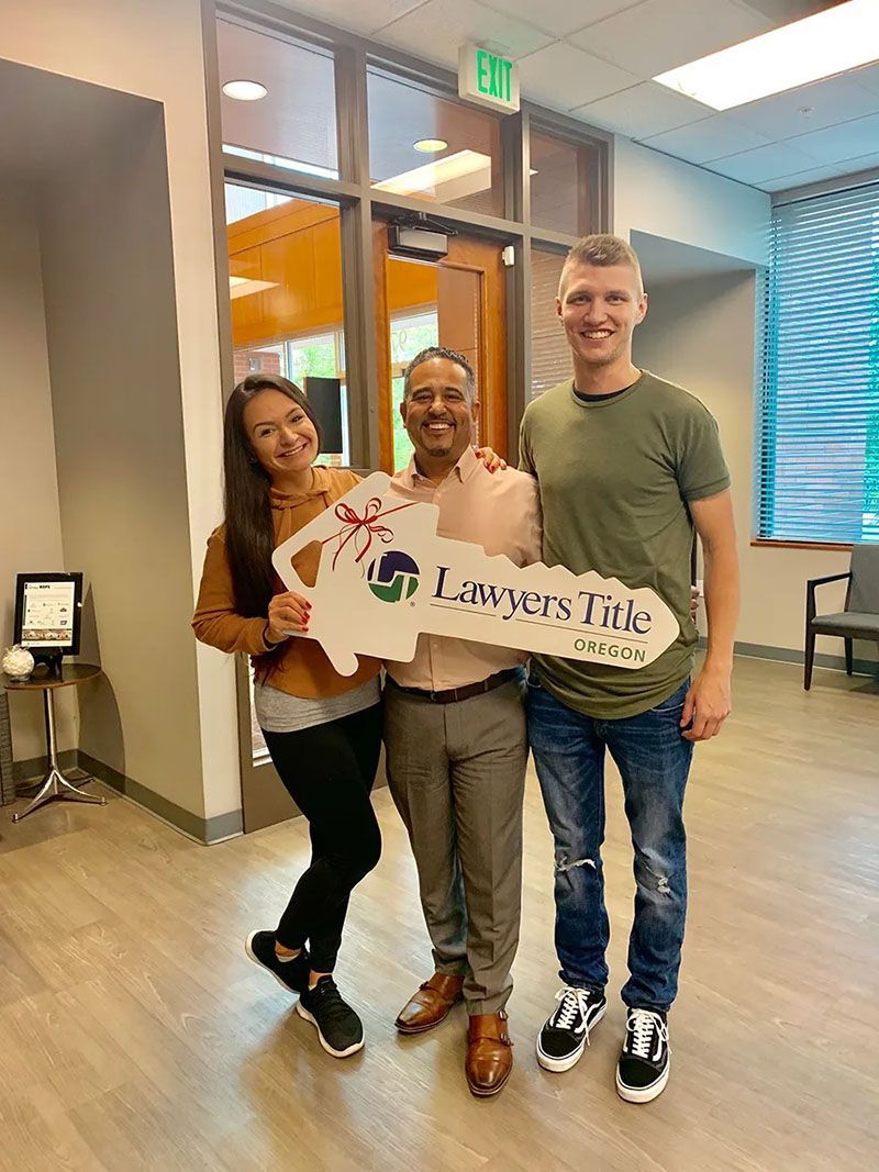 Three people holding a giant key inside a building. They are smiling.