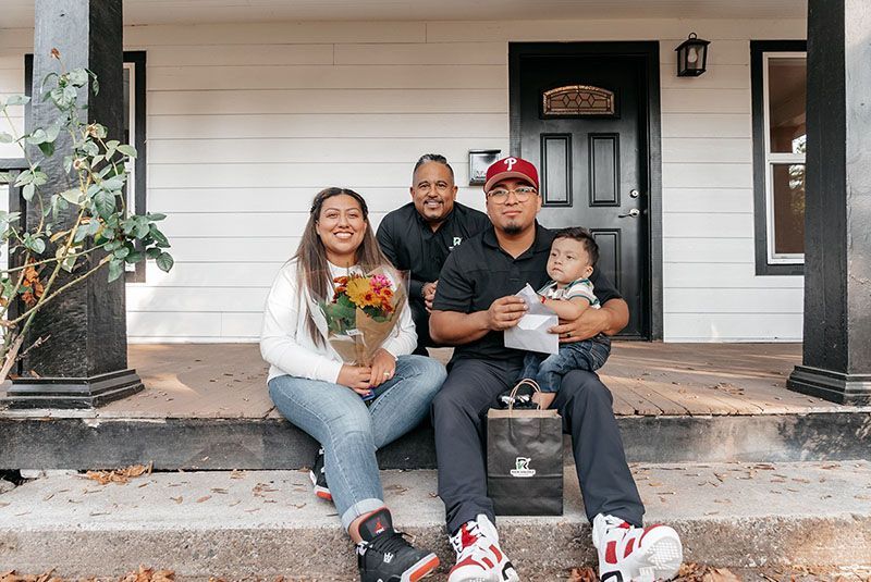 Family sitting on porch steps holding flowers and a baby.