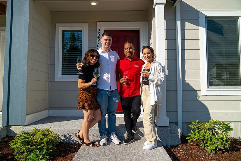 Four people standing in front of a house, smiling and holding glasses, celebrating.