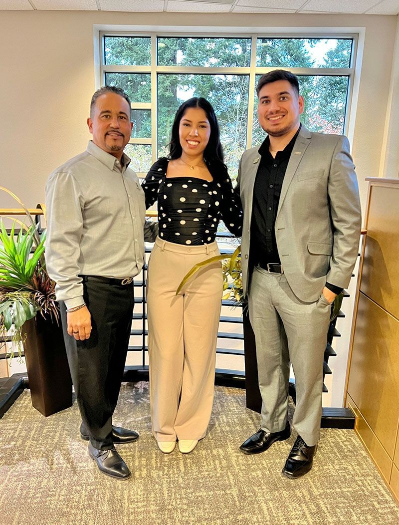 Three people standing together; woman in polka dots, flanked by men in button-downs and suit.