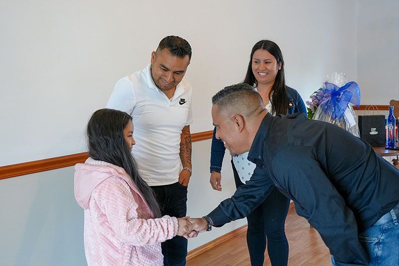 Man shakes hands with girl; two adults watch. Interior, bright room.
