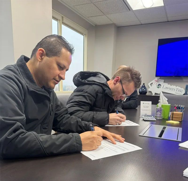 Two people seated at a table, signing documents in an office setting.