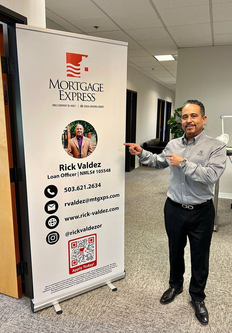 Man points at a Mortgage Express banner with his photo and contact info in an office setting.