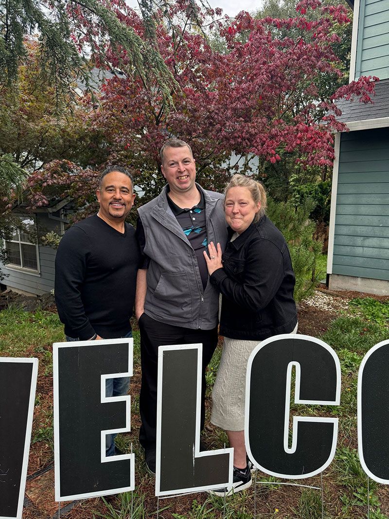 Three people stand in front of a house. A 