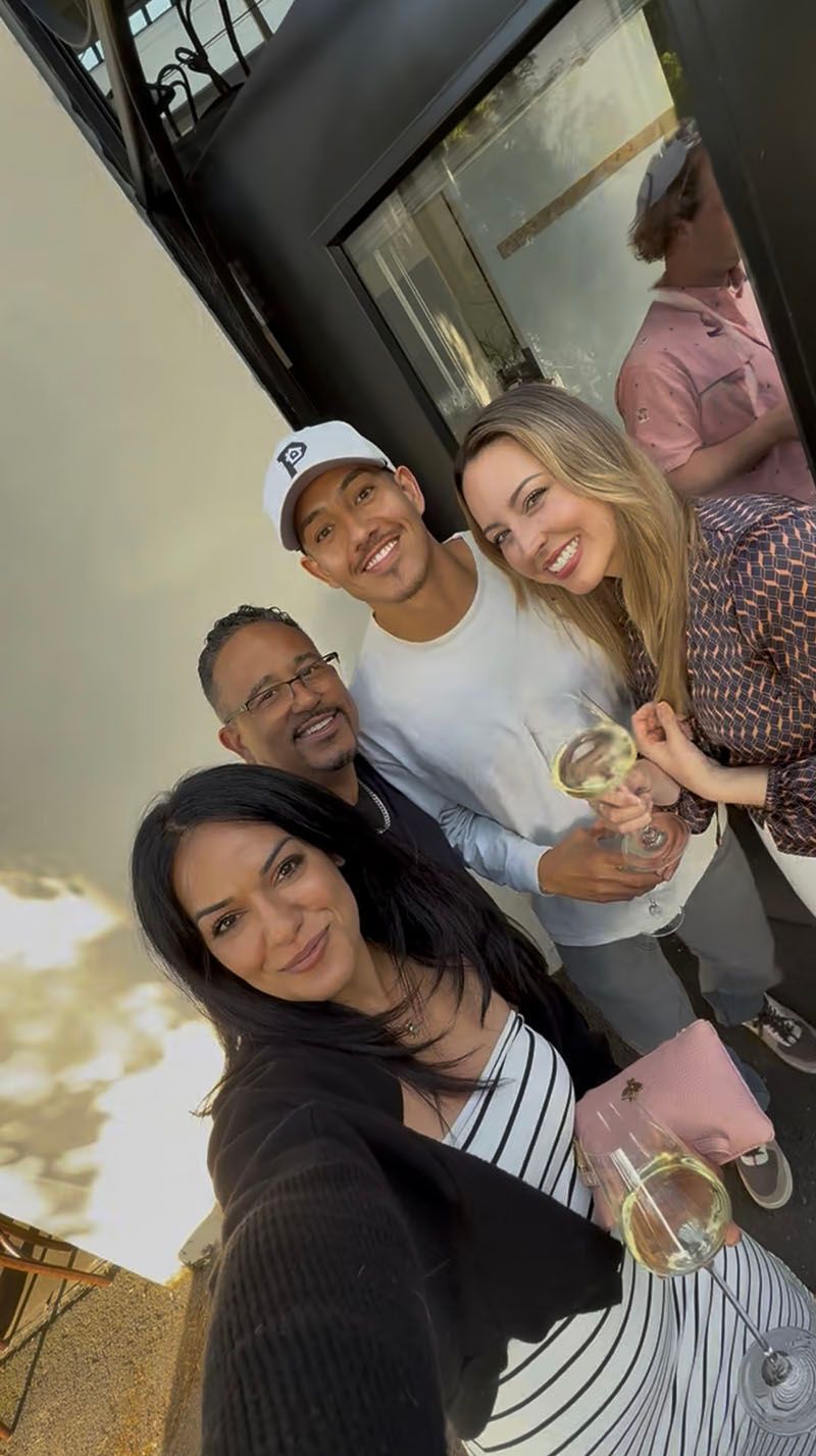 Group of people smiling, holding glasses, outdoors. Building in the background.
