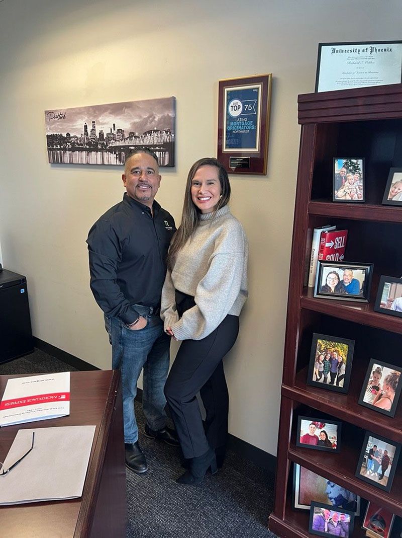 Man and woman standing next to each other in an office. They are smiling. Shelves in the background.