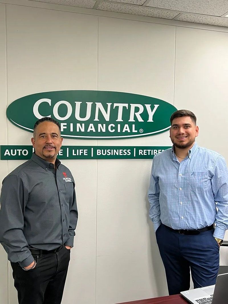 Two men standing in front of a Country Financial sign. One in grey shirt, other in blue shirt. Office setting.