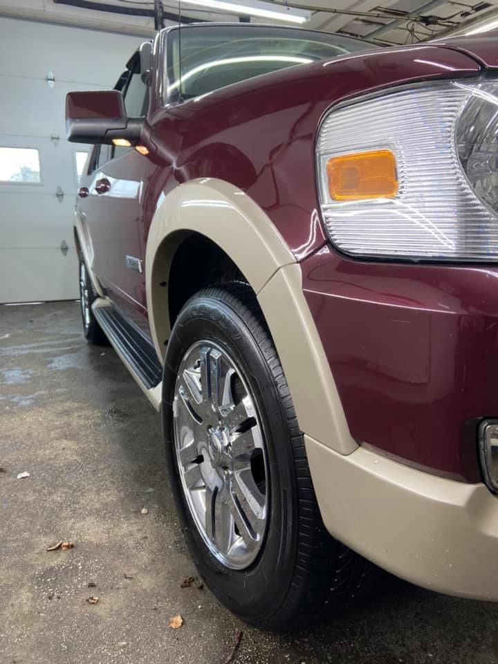 Maroon Ford Explorer with chrome wheels and tan fender flares in a garage.