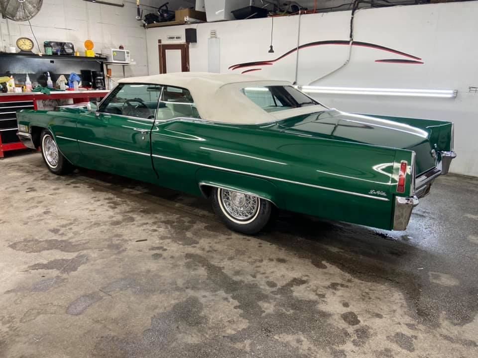 Green Cadillac convertible in a garage, with a beige top, shiny paint.