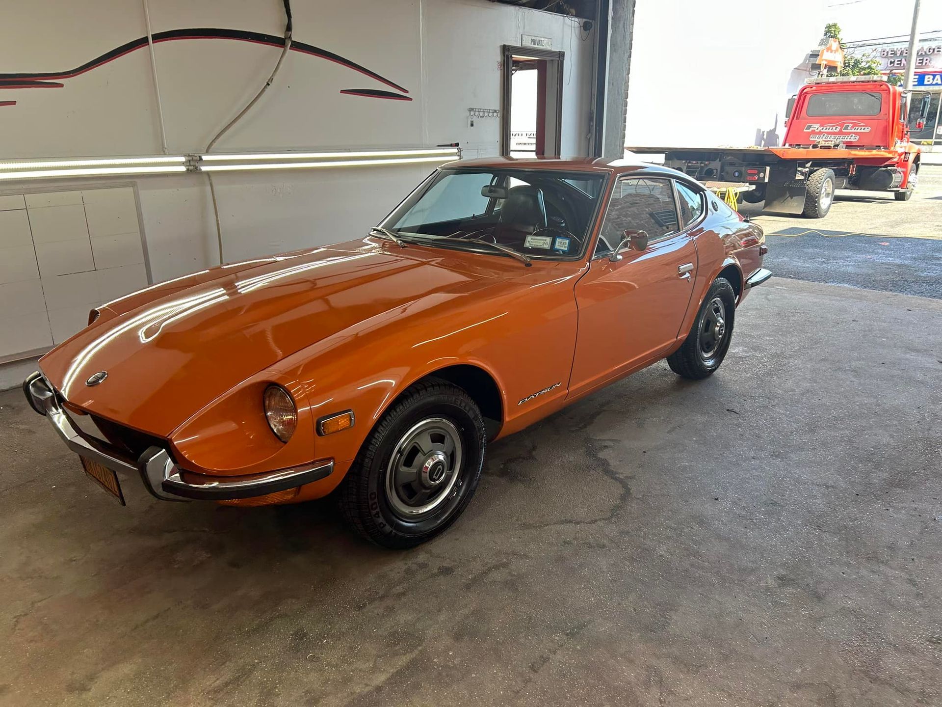 Orange Datsun 240Z sports car parked near a building. White stripe on the hood.