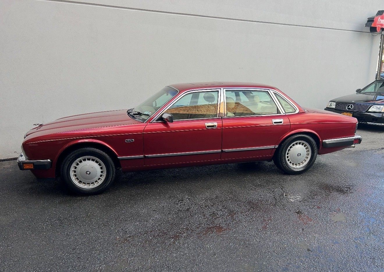 Red Jaguar sedan parked on a wet, gray surface next to a building.