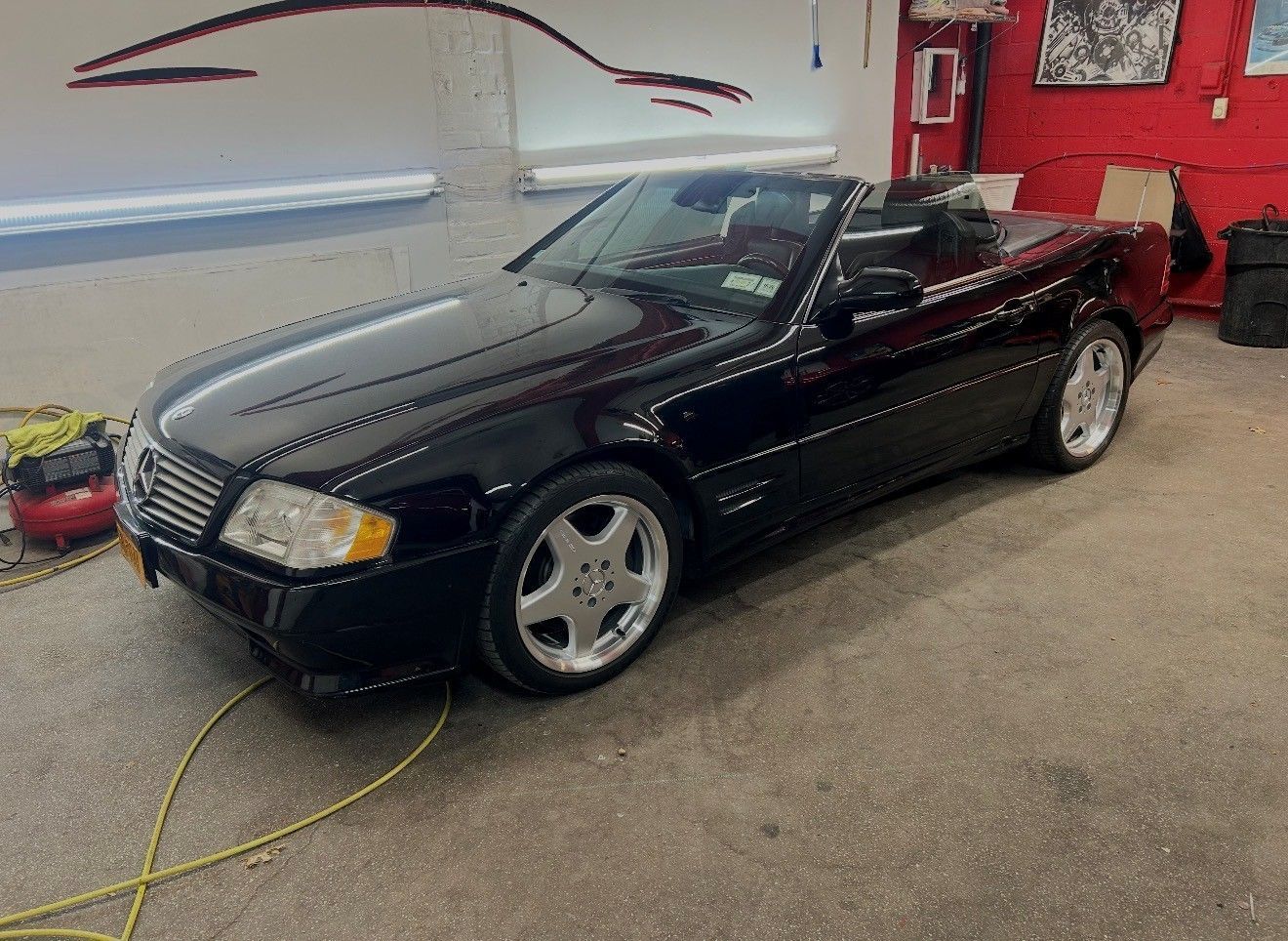 Black convertible Mercedes-Benz SL, top down, parked inside a garage.