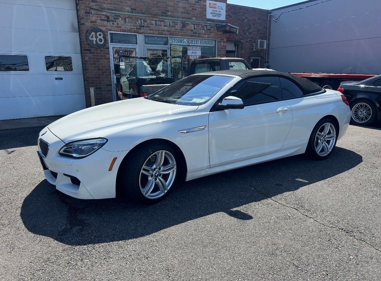White BMW convertible parked in front of an auto repair shop with a partially open garage door.