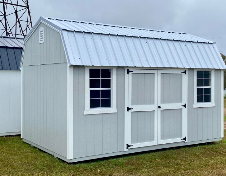 Gray barn-style shed with white trim, a metal roof, two windows, and double doors, set on grass.