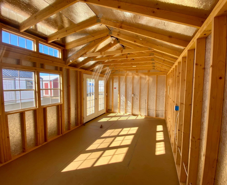 Interior of a shed under construction; wooden beams and studs, windows, and sunlight on the floor.