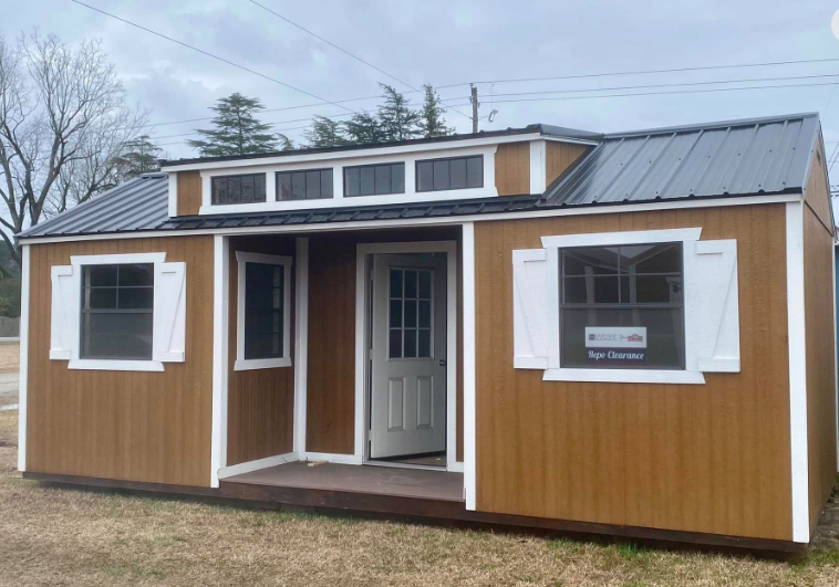 Brown tiny house with white trim, metal roof, and shutters.