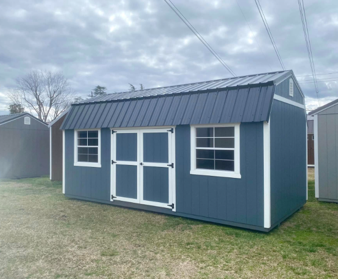 Blue storage shed with white trim, a metal roof, and two windows on display outside.