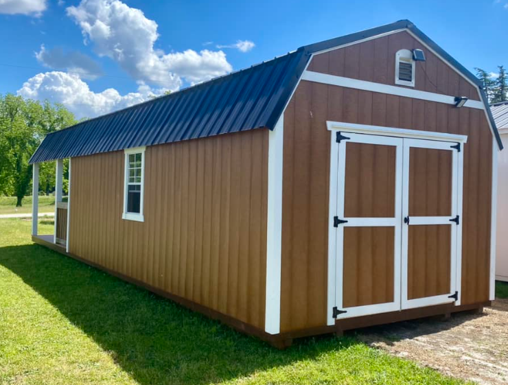 Brown shed with white trim, black roof, and small porch against a blue sky.