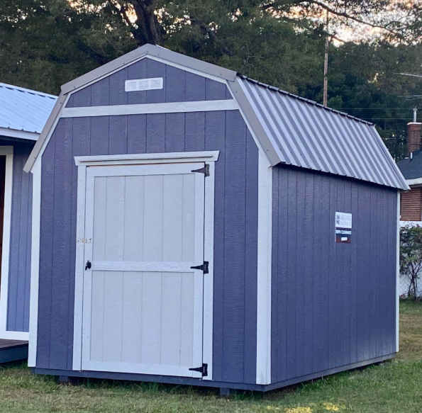 Blue and white barn-style shed with a metal roof on green grass.
