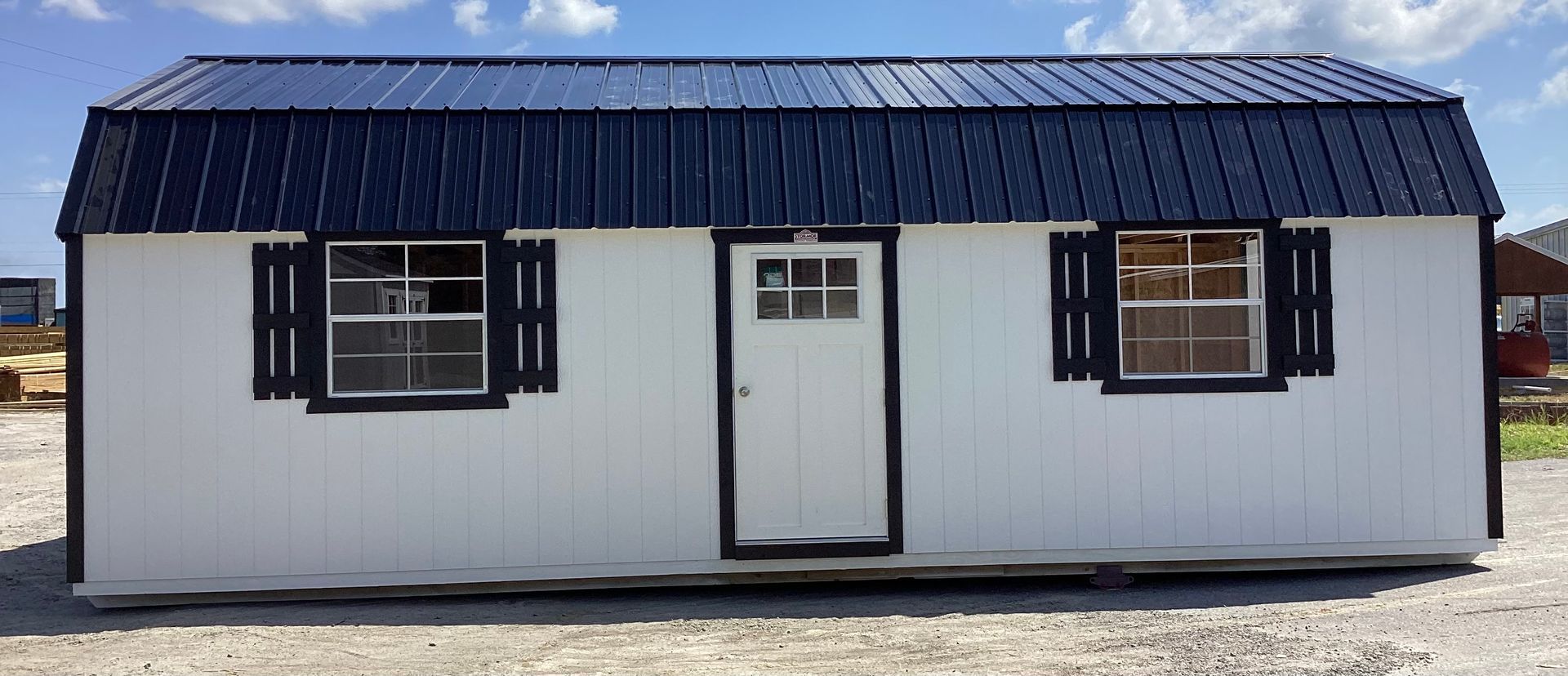 White shed with dark blue roof, shutters, and trim against a blue sky.